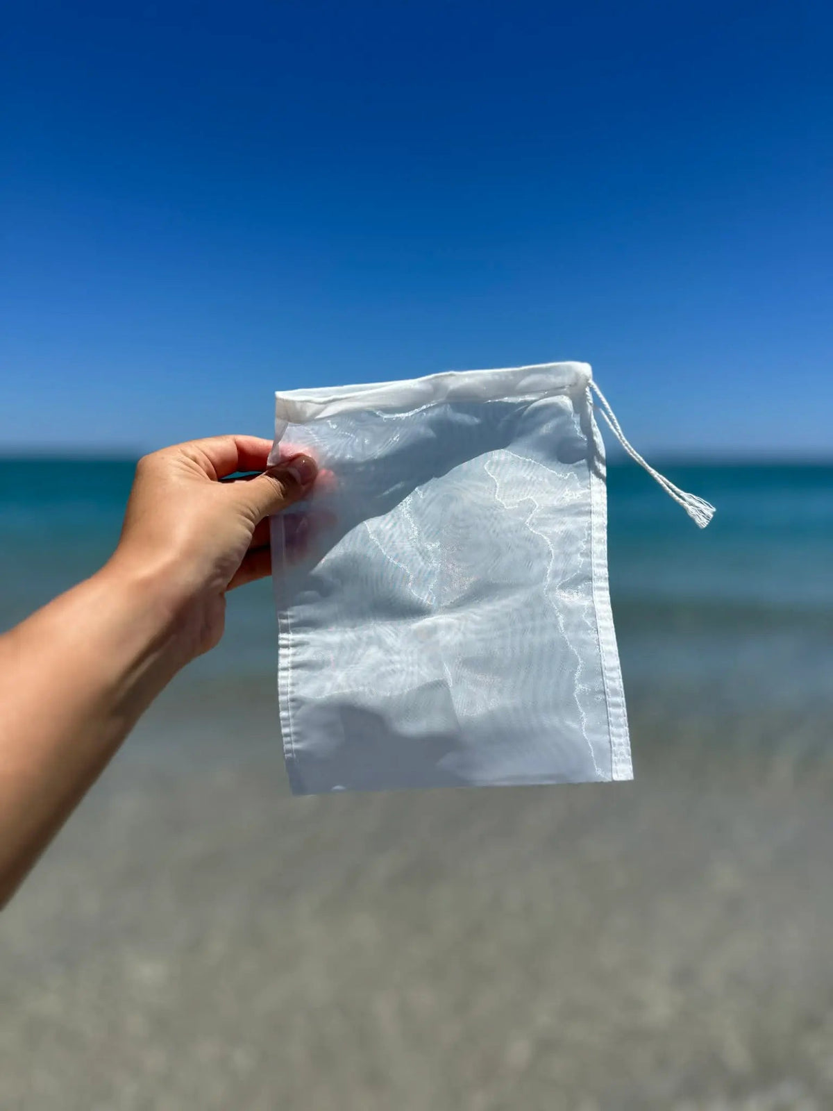 Hand holding a nylon kava strainer bag against the sea
